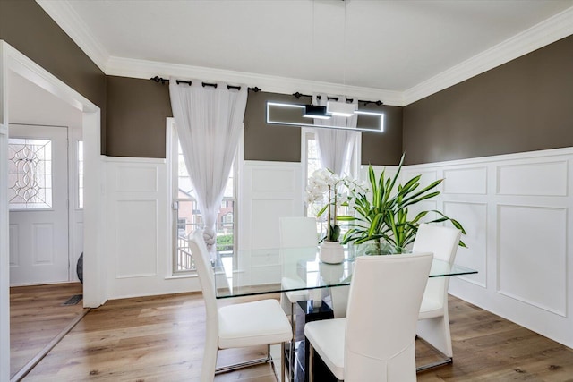 dining space featuring light wood finished floors, crown molding, and a decorative wall