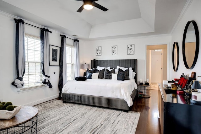 bedroom featuring a tray ceiling, crown molding, wood finished floors, and baseboards