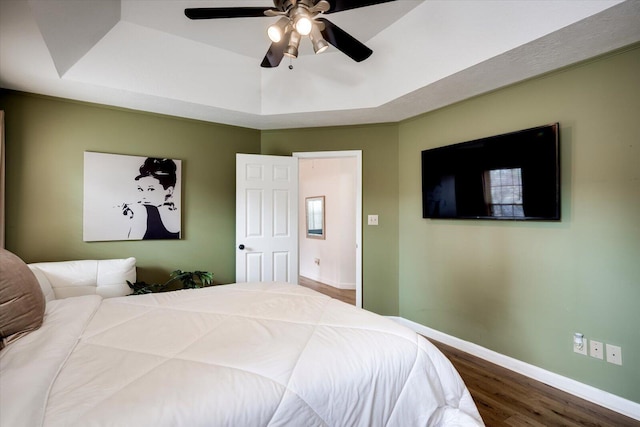 bedroom featuring a tray ceiling, wood finished floors, baseboards, and ceiling fan