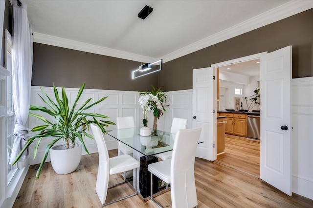 dining room with a decorative wall, crown molding, wainscoting, and light wood finished floors