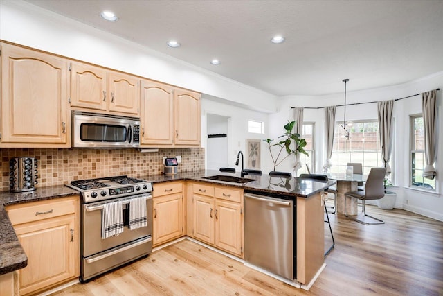 kitchen with a sink, a peninsula, light brown cabinets, and stainless steel appliances