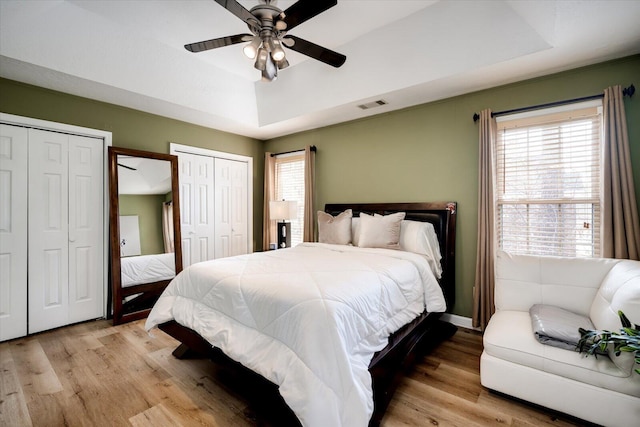 bedroom featuring a tray ceiling, visible vents, two closets, and light wood-type flooring