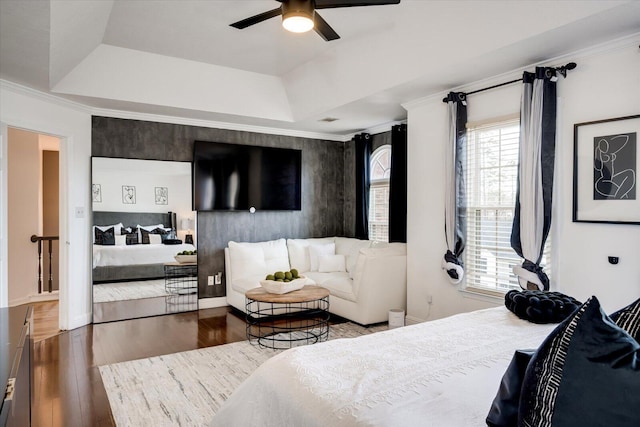 bedroom with a tray ceiling, baseboards, wood finished floors, and crown molding