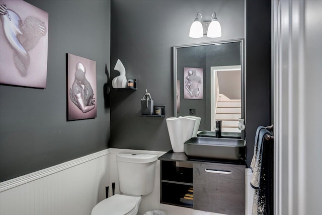 bathroom featuring vanity, toilet, and a wainscoted wall