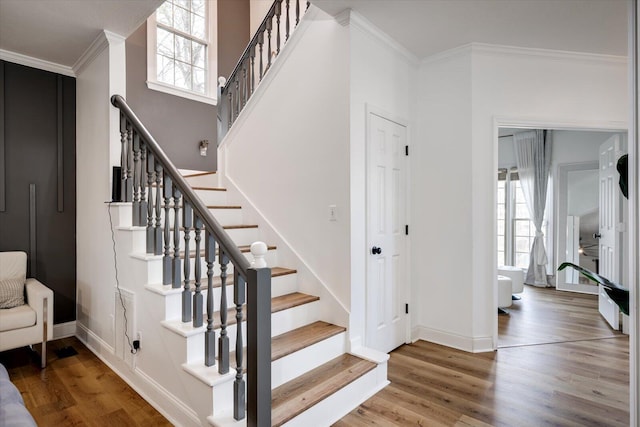 stairway featuring baseboards, a healthy amount of sunlight, wood finished floors, and ornamental molding