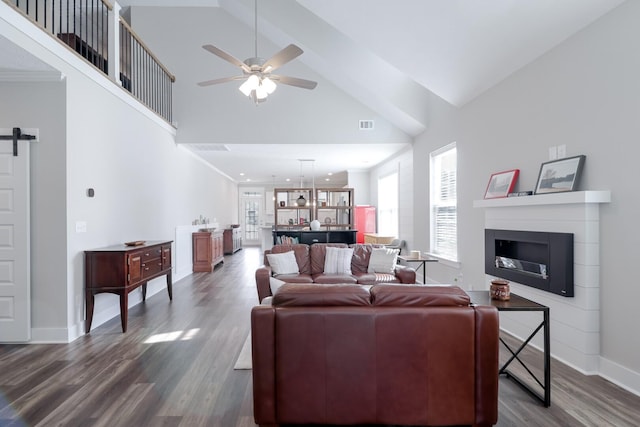 living area with baseboards, a ceiling fan, dark wood-style floors, high vaulted ceiling, and a glass covered fireplace
