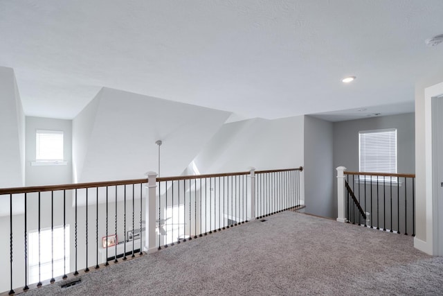 hallway featuring an upstairs landing, visible vents, baseboards, and carpet floors