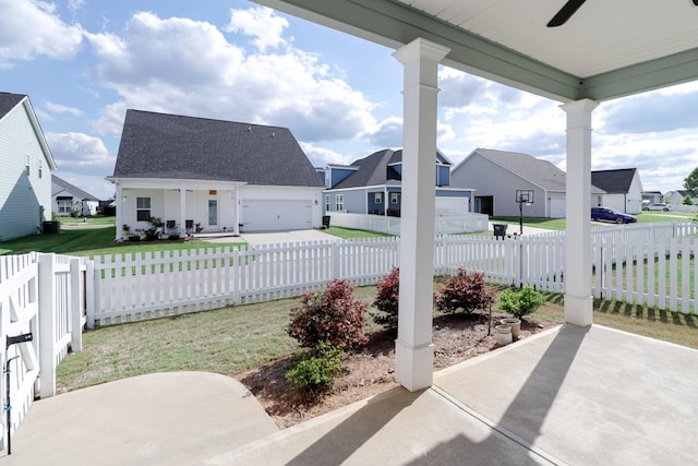 view of patio featuring a fenced front yard, ceiling fan, a garage, concrete driveway, and a residential view