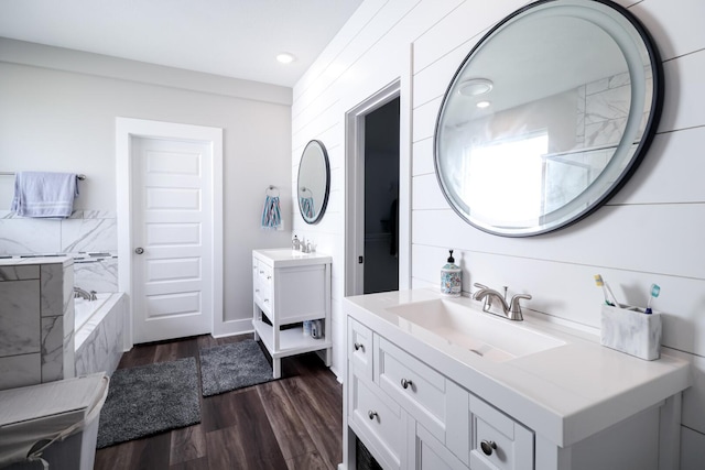 bathroom featuring a sink, two vanities, wood finished floors, and a bath