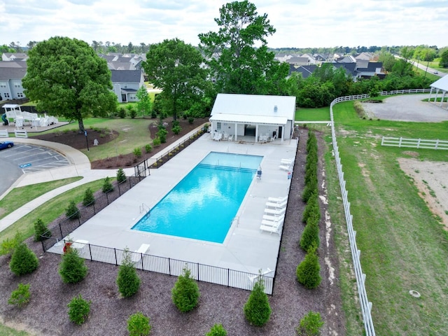 community pool featuring a residential view, a patio area, fence, and an outbuilding