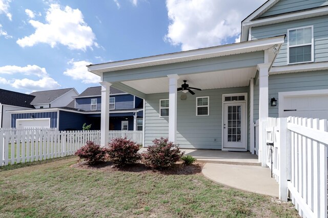 entrance to property with a porch, fence, a lawn, and ceiling fan