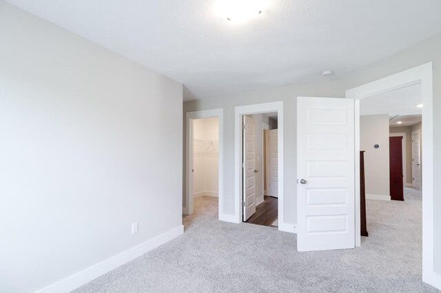 unfurnished bedroom featuring a closet, a walk in closet, carpet, and baseboards