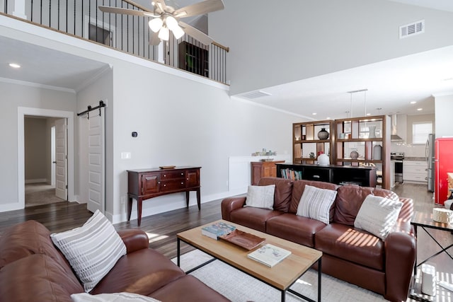 living room with crown molding, a ceiling fan, visible vents, a barn door, and wood finished floors