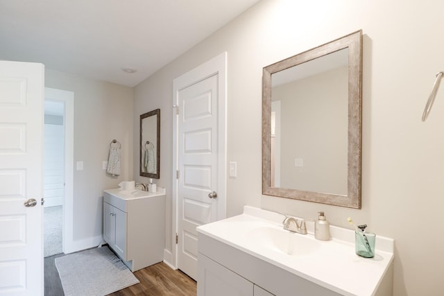 bathroom with wood finished floors, two vanities, a sink, and baseboards