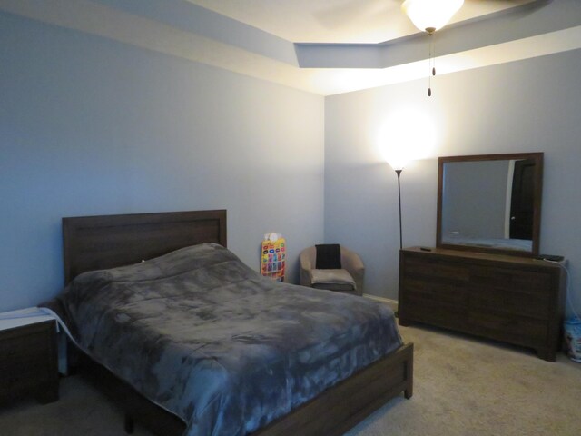 carpeted bedroom with ceiling fan and a tray ceiling