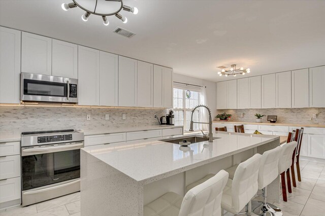 kitchen with a sink, visible vents, appliances with stainless steel finishes, decorative backsplash, and a center island with sink