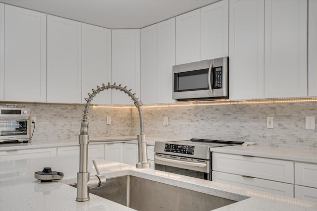 kitchen with white cabinets, light stone counters, stainless steel appliances, and decorative backsplash