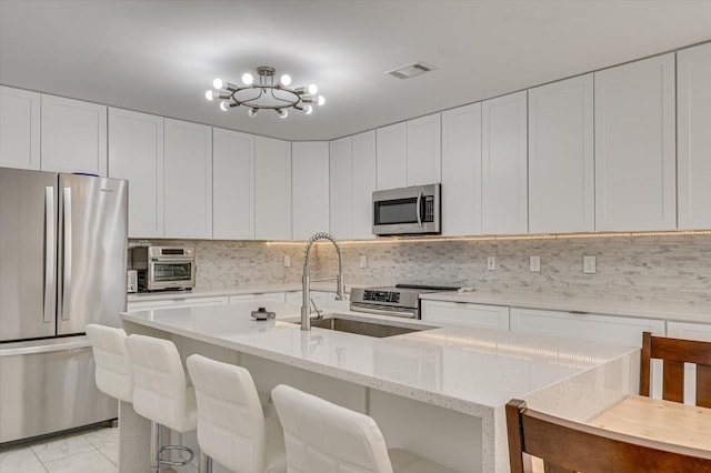 kitchen featuring stainless steel appliances, visible vents, decorative backsplash, a sink, and light stone countertops