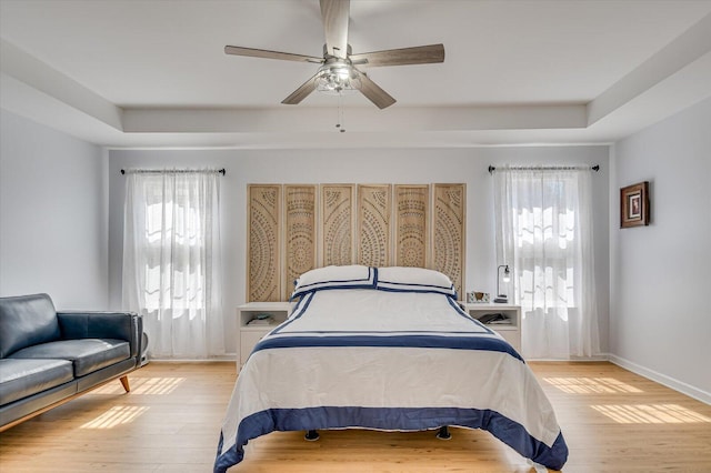 bedroom with a ceiling fan, a raised ceiling, baseboards, and light wood finished floors