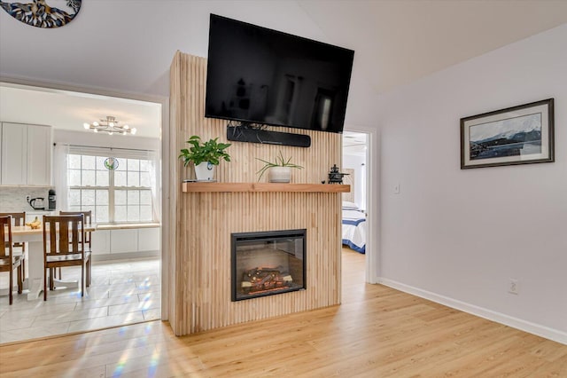 living area with a glass covered fireplace, light wood-style flooring, and baseboards