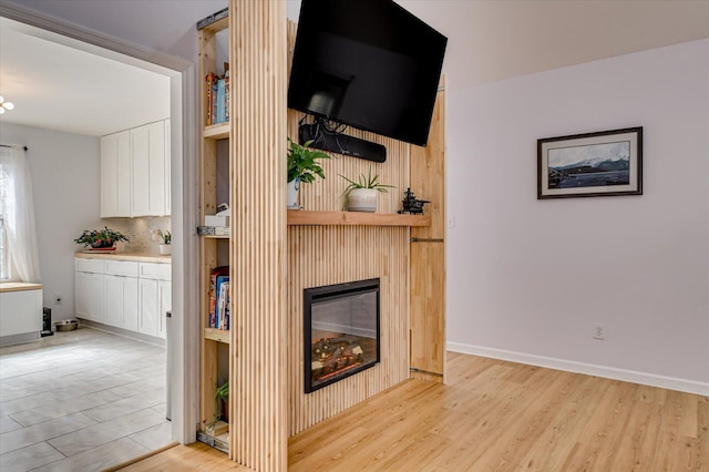 unfurnished living room featuring light wood-style floors, a glass covered fireplace, and baseboards