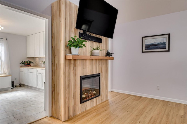 unfurnished living room featuring light wood finished floors, a glass covered fireplace, and baseboards