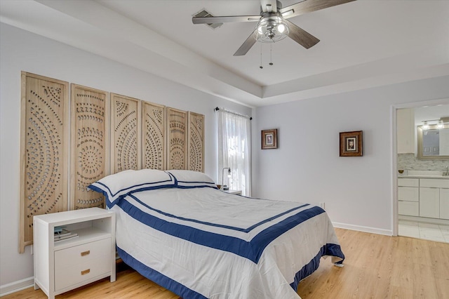 bedroom with light wood-type flooring, a ceiling fan, baseboards, and connected bathroom