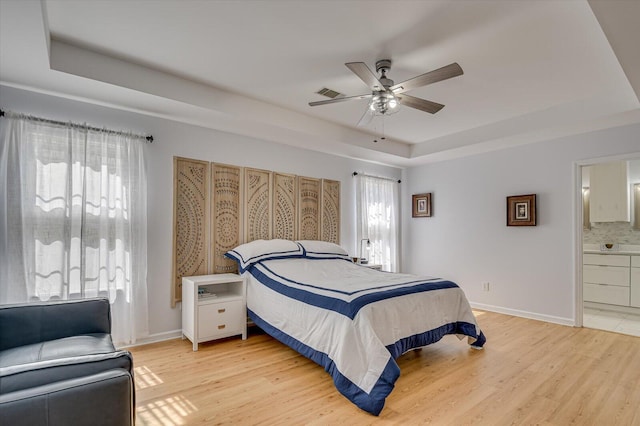 bedroom with light wood finished floors, multiple windows, and a tray ceiling