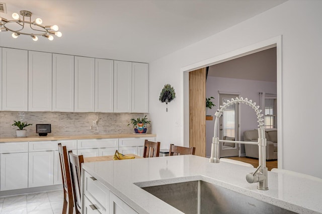 kitchen featuring tasteful backsplash, light stone countertops, and white cabinets