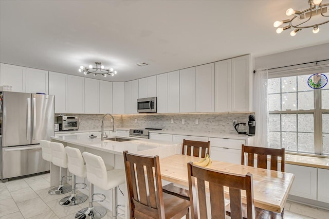 kitchen with decorative backsplash, appliances with stainless steel finishes, light countertops, a chandelier, and a sink