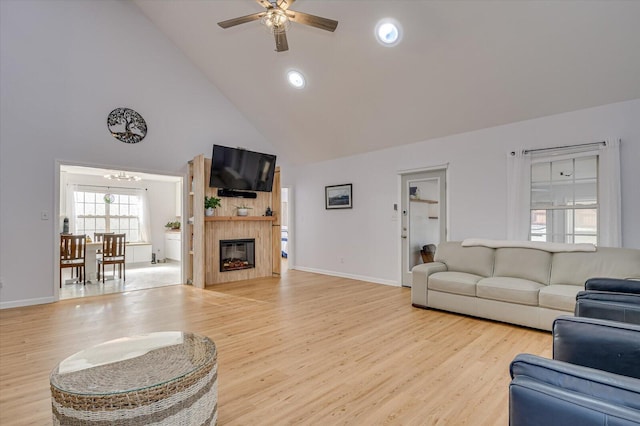 living area featuring light wood-type flooring, ceiling fan, high vaulted ceiling, and a glass covered fireplace