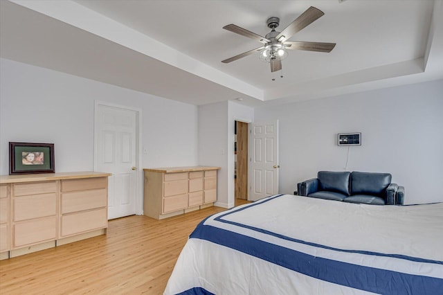 bedroom featuring ceiling fan, a tray ceiling, and light wood-style flooring