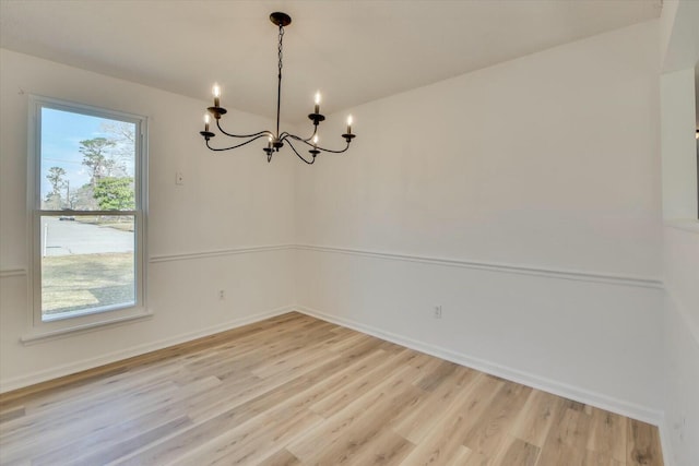 spare room with a notable chandelier, baseboards, and light wood finished floors