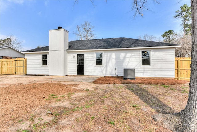 back of house with a shingled roof, central air condition unit, fence, and a chimney