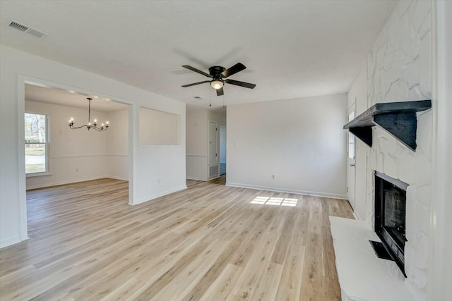 unfurnished living room with visible vents, baseboards, light wood-style flooring, a high end fireplace, and ceiling fan with notable chandelier