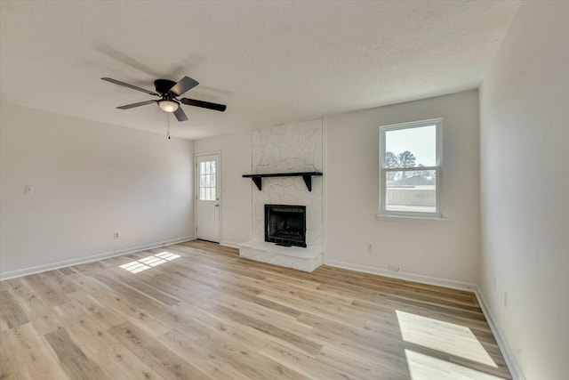 unfurnished living room featuring a ceiling fan, light wood-style flooring, a fireplace, and a textured ceiling