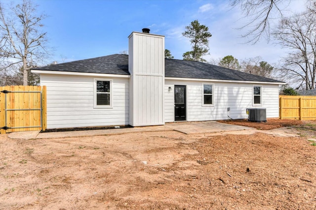 rear view of property featuring a gate, fence, roof with shingles, central AC unit, and a chimney