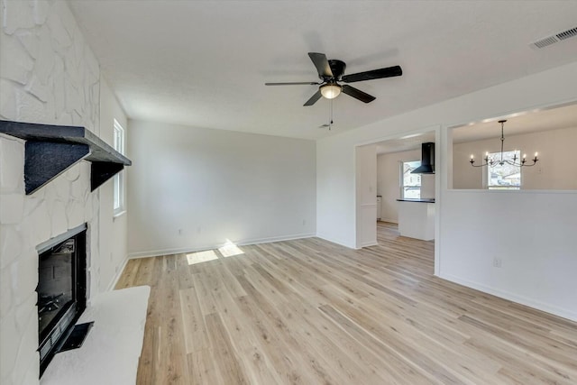 unfurnished living room with visible vents, a large fireplace, baseboards, ceiling fan with notable chandelier, and light wood-style floors