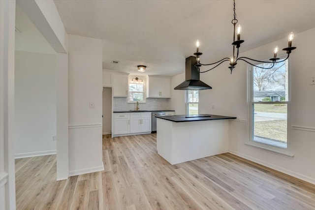 kitchen featuring dark countertops, tasteful backsplash, wall chimney range hood, an inviting chandelier, and white cabinetry