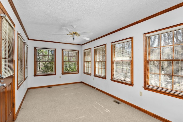 carpeted empty room featuring ceiling fan, crown molding, and a textured ceiling