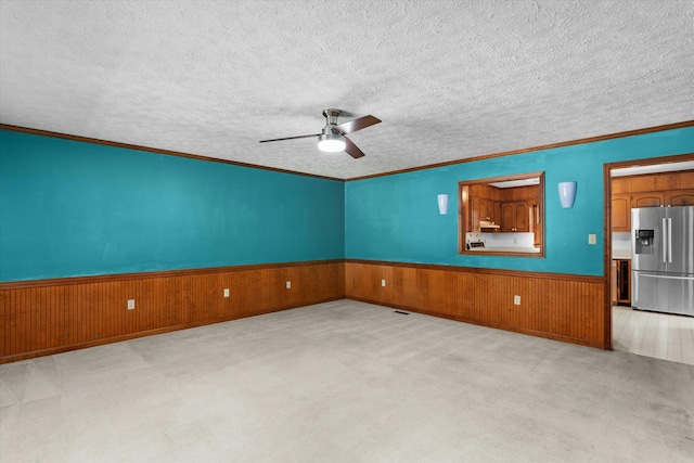 carpeted spare room with a textured ceiling, ornamental molding, wood walls, and ceiling fan