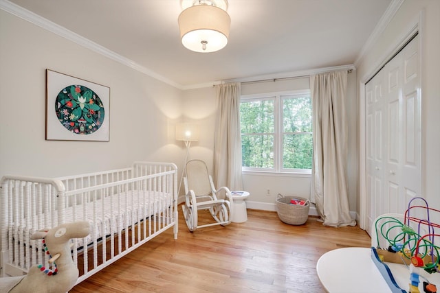 bedroom featuring crown molding, light wood-style flooring, a closet, baseboards, and a nursery area