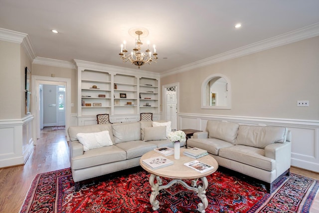 living area with ornamental molding, a chandelier, light wood-type flooring, wainscoting, and a decorative wall