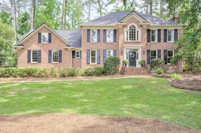 colonial inspired home featuring a front lawn, brick siding, a chimney, and roof with shingles