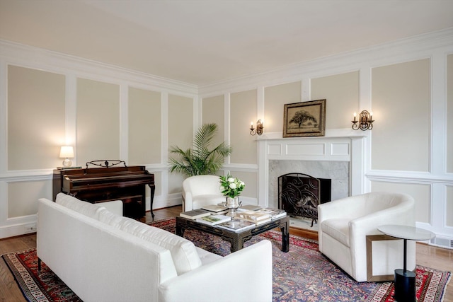 living area with a fireplace, wood finished floors, a decorative wall, and ornamental molding