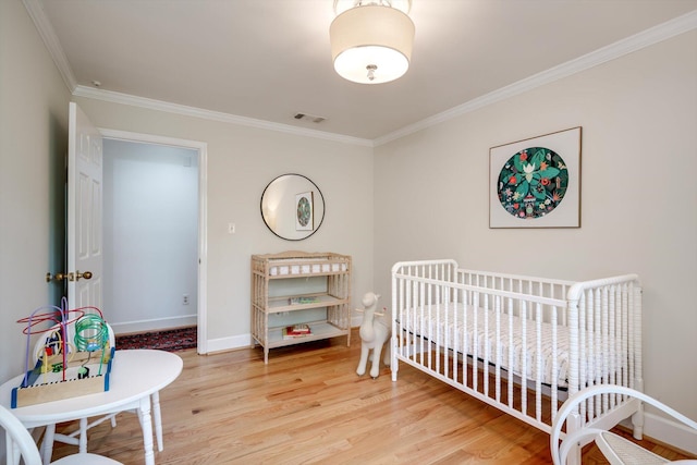 bedroom with crown molding, wood finished floors, baseboards, and a crib