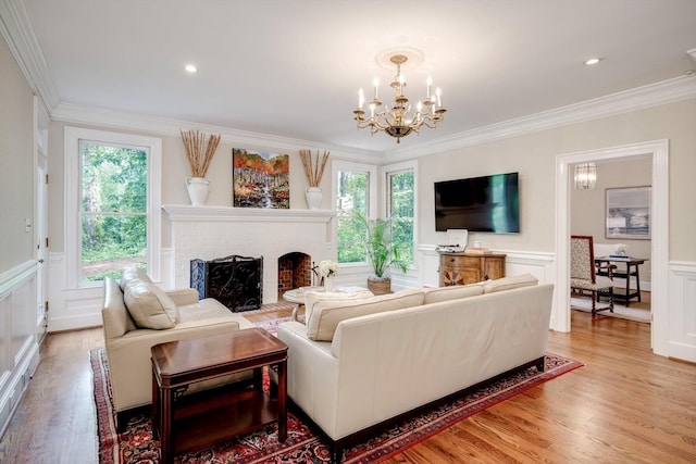 living room with a chandelier, ornamental molding, light wood finished floors, a fireplace, and a wainscoted wall