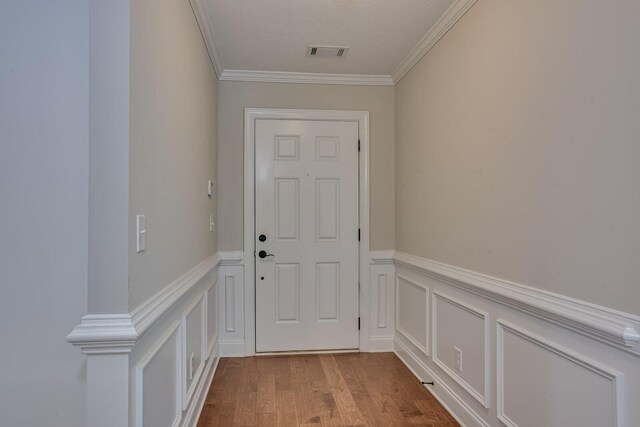 doorway to outside with light wood-type flooring, a textured ceiling, and ornamental molding