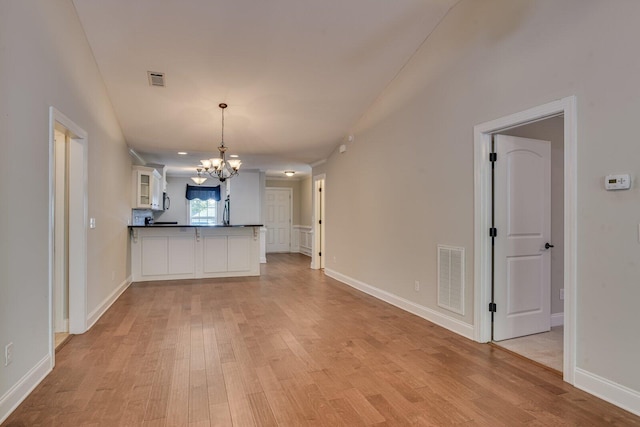 kitchen with white cabinets, decorative light fixtures, a notable chandelier, and light hardwood / wood-style floors