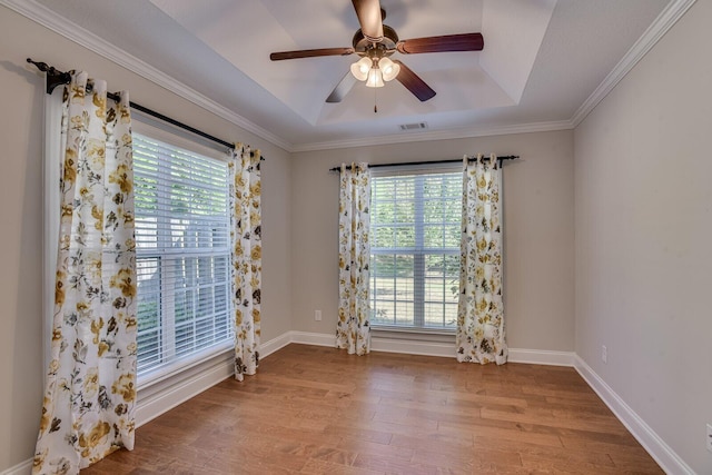 empty room featuring a tray ceiling, ceiling fan, light hardwood / wood-style flooring, and ornamental molding